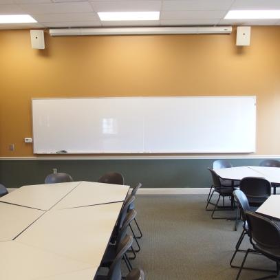 Modular tables and chairs with projection screen and speakers mounted on wall.